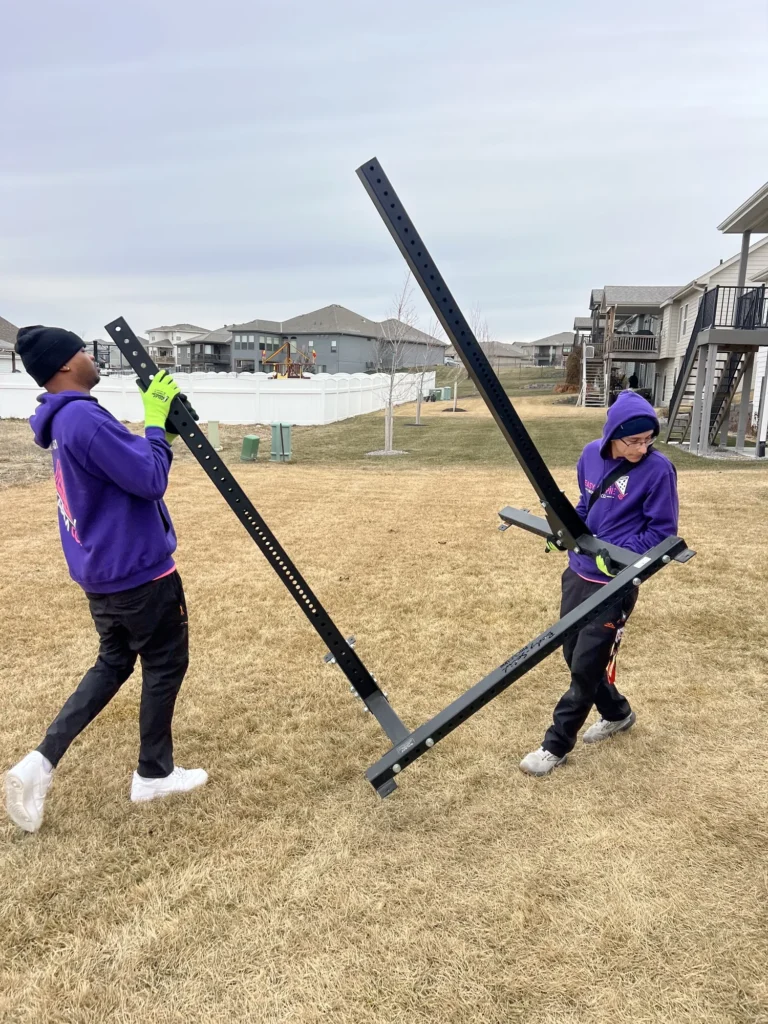 Easy As Pie movers carrying metal bed frame rails outside