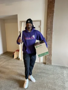 Smiling Easy As Pie mover carrying a moving box into a home