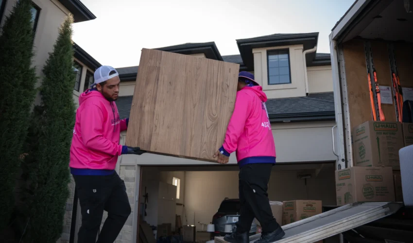 Two Easy as Pie movers in bright pink uniforms carrying a large wooden cabinet during a residential move in Omaha, showing their professional packing and long-distance moving service. Piano Movers Omaha: Safe Instrument Moving Experts