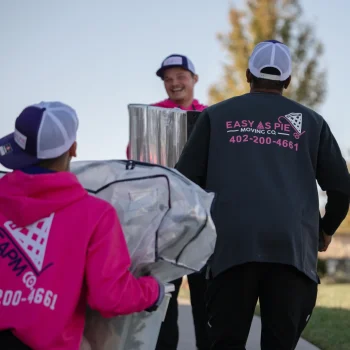 Omaha movers from Easy as Pie carrying wrapped household items while working together during a local move.