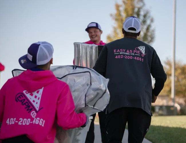 Omaha movers from Easy as Pie carrying wrapped household items while working together during a local move.