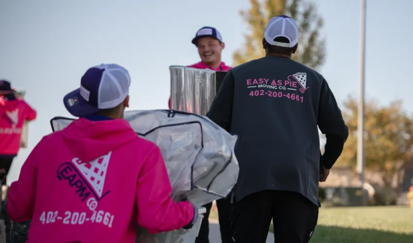 Omaha movers from Easy as Pie carrying wrapped household items while working together during a local move.