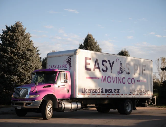 Bright pink Easy As Pie Moving Co truck helping a family moving to Omaha with family in a residential area