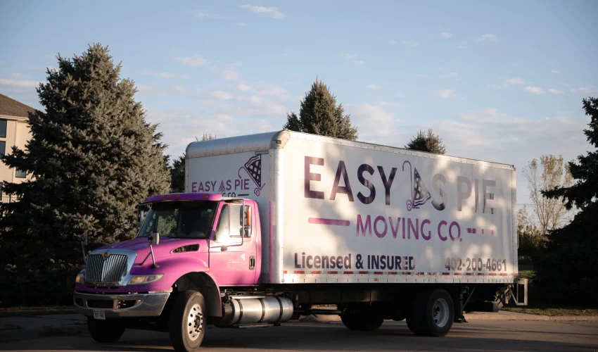 Bright pink Easy As Pie Moving Co truck helping a family moving to Omaha with family in a residential area