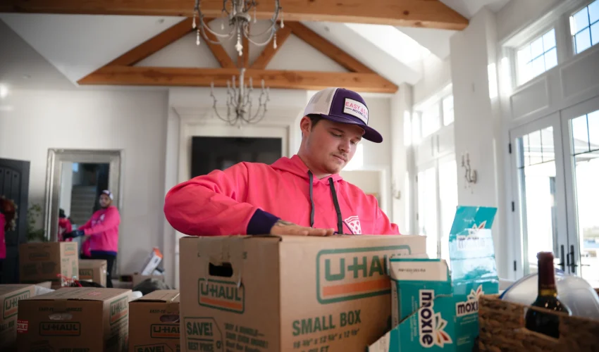 Local overs Omaha Easy As Pie crew packing boxes during a move, showing a mover sealing a U-Haul box as part of a moving checklist Omaha families use for smooth moving day prep. Senior movers Omaha professionally packing belongings for elderly woman's assisted living relocation
