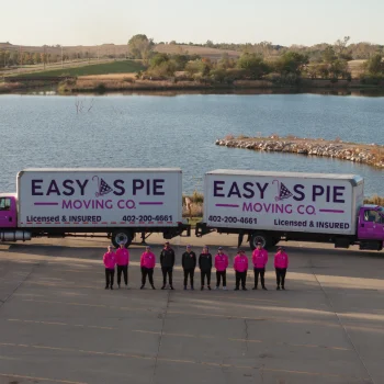 Easy as Pie Moving Co. team standing in front of two branded trucks near a lake in Omaha, showcasing their professional long-distance moving and packing services. out of state move to Omaha