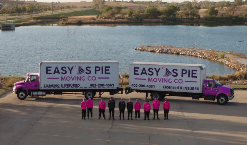 Easy as Pie Moving Co. team standing in front of two branded trucks near a lake in Omaha, showcasing their professional long-distance moving and packing services.